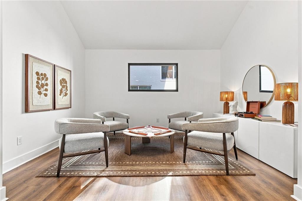 Staged sitting room with upholstered chairs, a low coffee table, patterned rug, and hardwood floors.