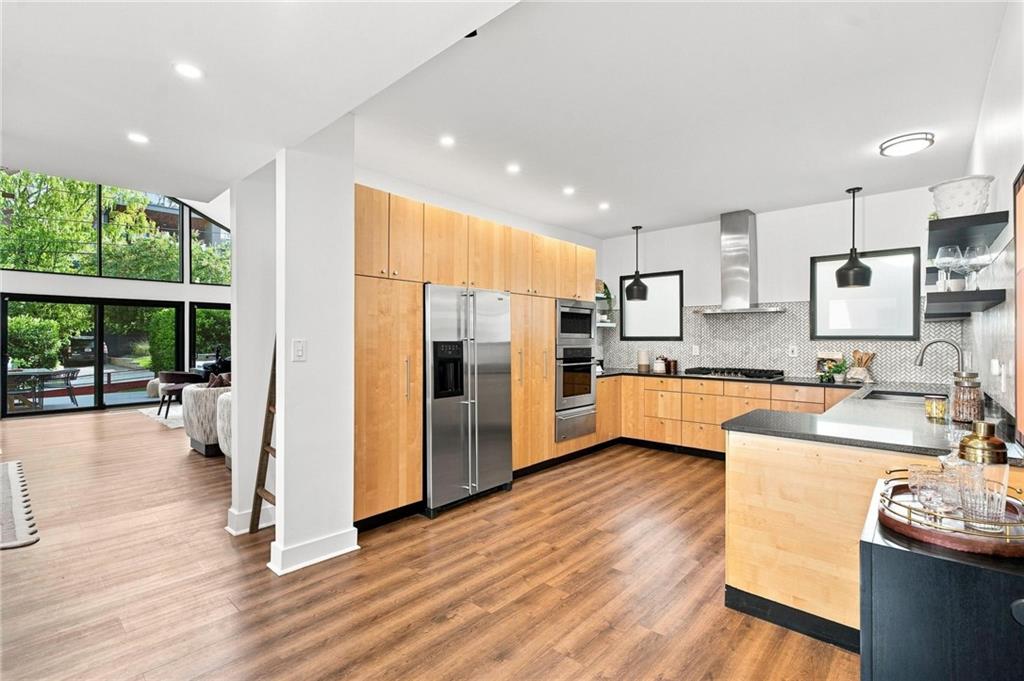 Open-plan kitchen with light wood cabinets, stainless steel appliances, and a large island beside floor-to-ceiling windows.