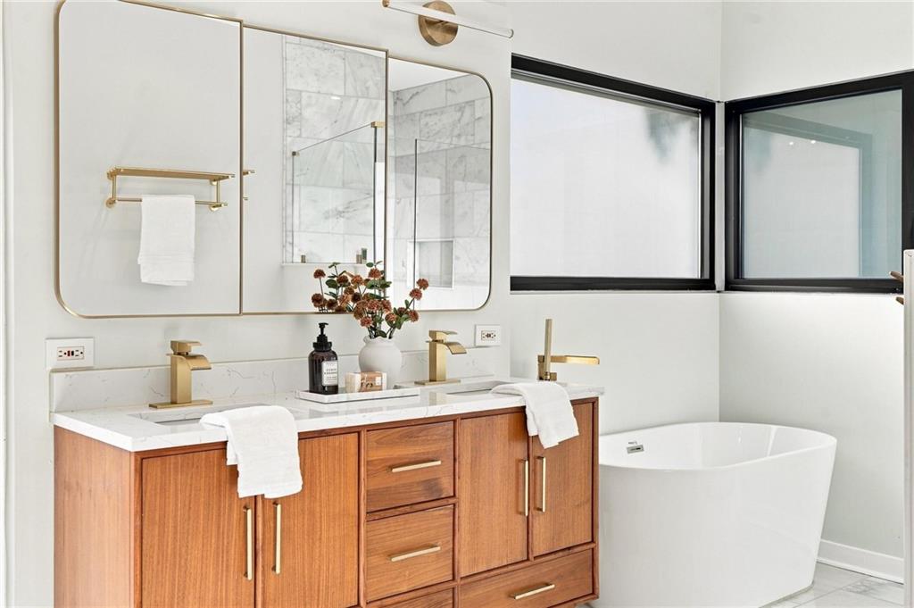 Modern bathroom with a walnut double vanity, gold fixtures, and a freestanding tub.