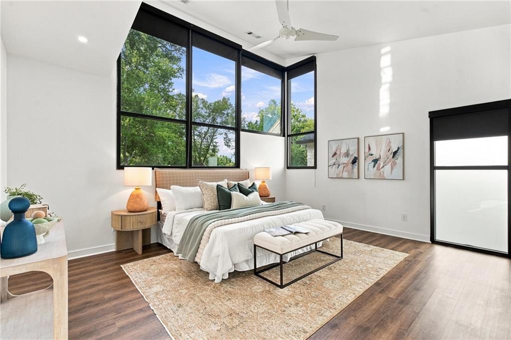 Bedroom with a king bed beneath tall black-framed windows overlooking trees.