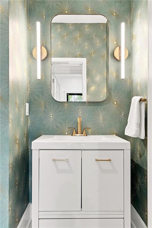 Bathroom vanity with pale green starburst wallpaper, brass fixtures, and a rounded rectangular mirror.