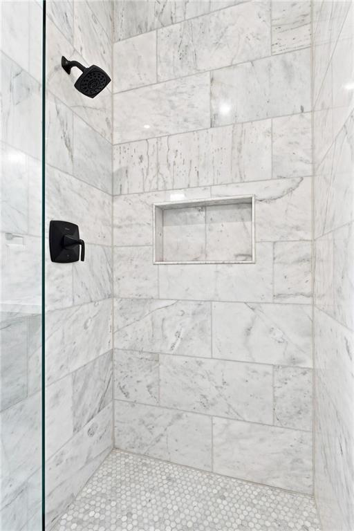 Walk-in shower with marble tile, a recessed niche, black fixtures, and hexagonal mosaic flooring.