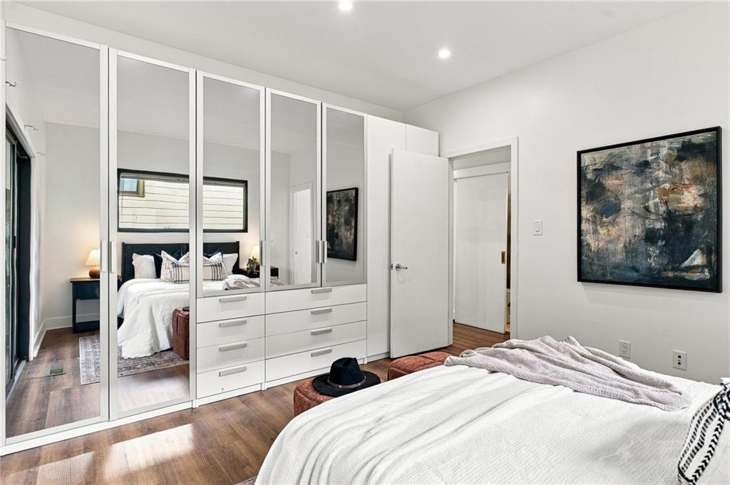 Bedroom with mirrored wardrobe, white bedding, dark wood floors, and abstract art.