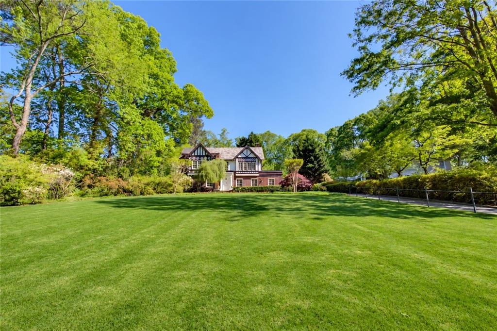 Tudor-style brick house beyond a broad lawn, framed by mature leafy trees.