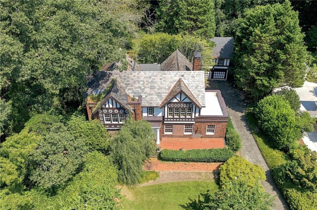 Aerial view of a brick Tudor home with steep shingle roofs, framed by mature trees and landscaped grounds.