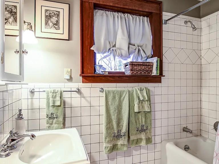 Tiled bathroom with a bathtub, white sink, green towels, and a wood-trimmed window.