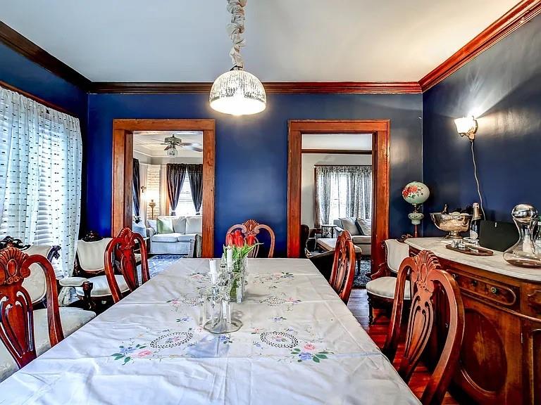 Dining room with a floral-covered table, carved wooden chairs, and deep blue walls.