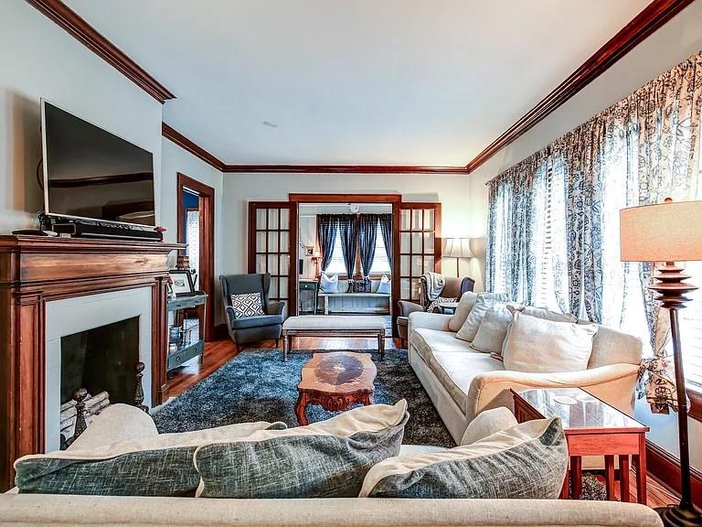 Living room with a white sofa, fireplace, television, and tall curtained windows.