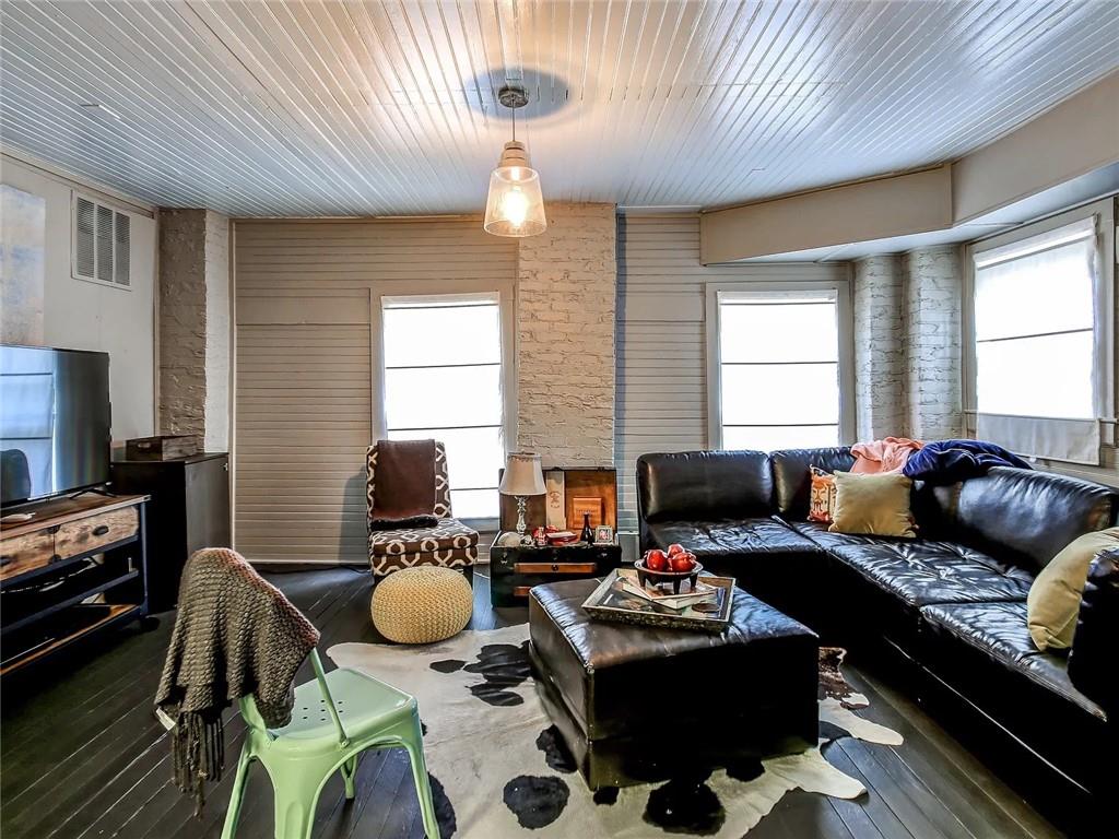 Living room with a black leather sectional, cowhide-pattern rug, and white-painted brick walls.