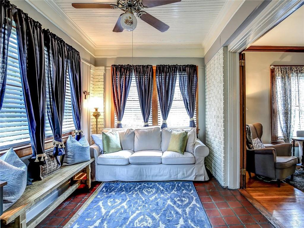 Living room with a white sofa, dark blue curtains, terracotta tile floors, and a patterned blue rug.