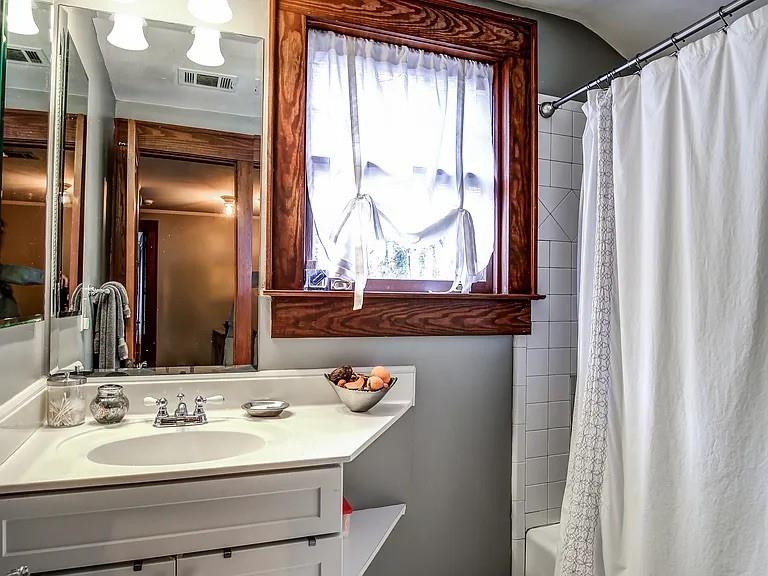 Bathroom with a white vanity, wood-trimmed window, and tiled tub-shower.