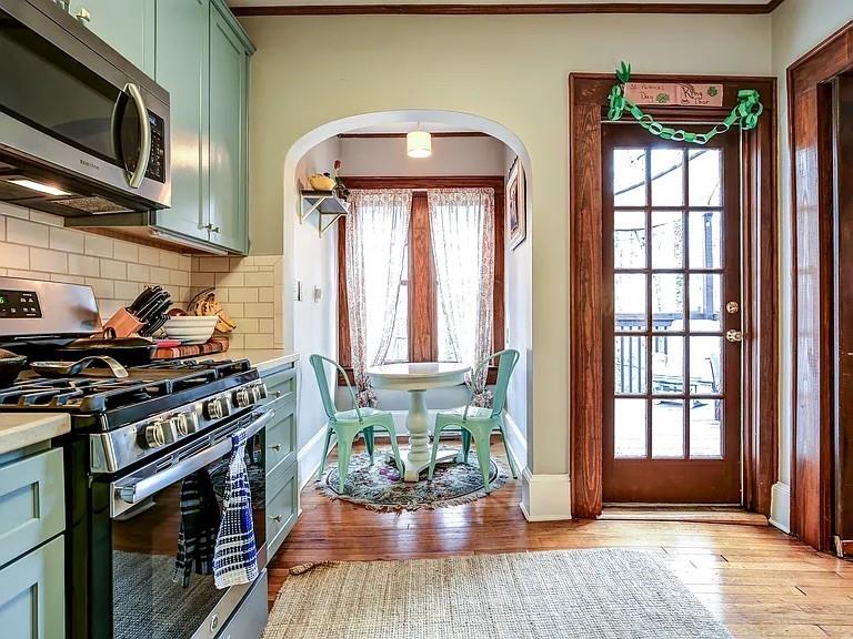 Kitchen with pale green cabinets, stainless steel appliances, and a breakfast nook by a wood-framed glass door.