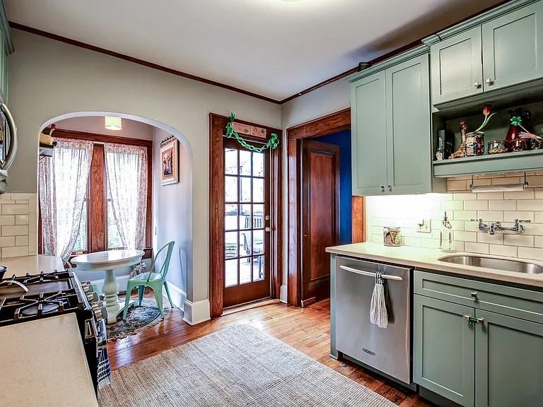 Kitchen with sage green cabinets and a dining nook beyond an arched opening.