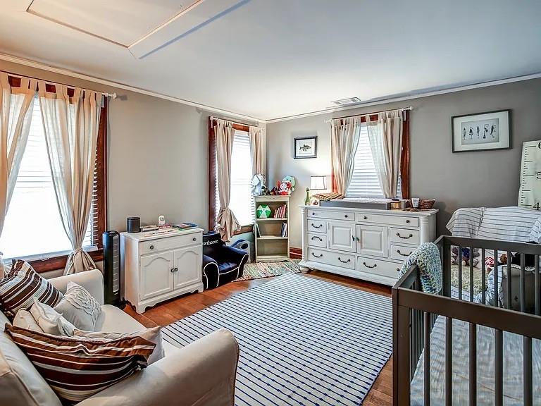 Furnished nursery with a dark wooden crib, white dresser, and striped rug.
