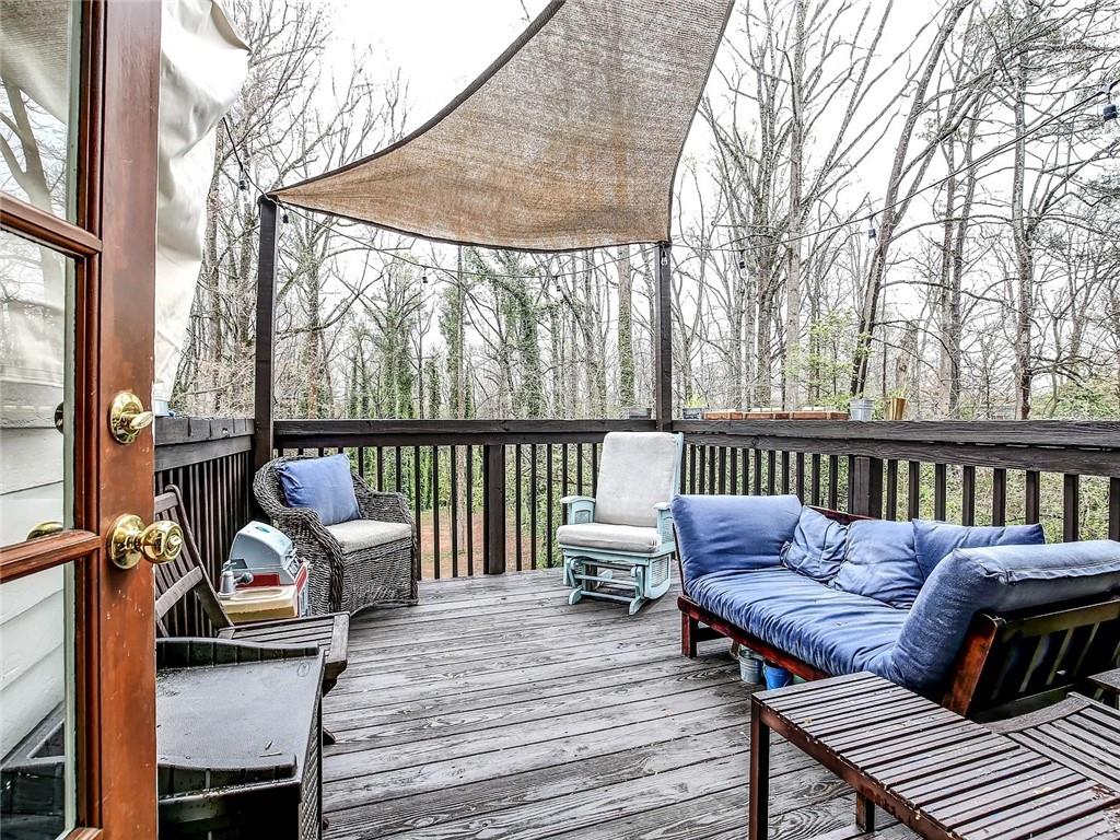 Furnished wooden deck with blue-cushioned seating and a shade sail overlooking trees.