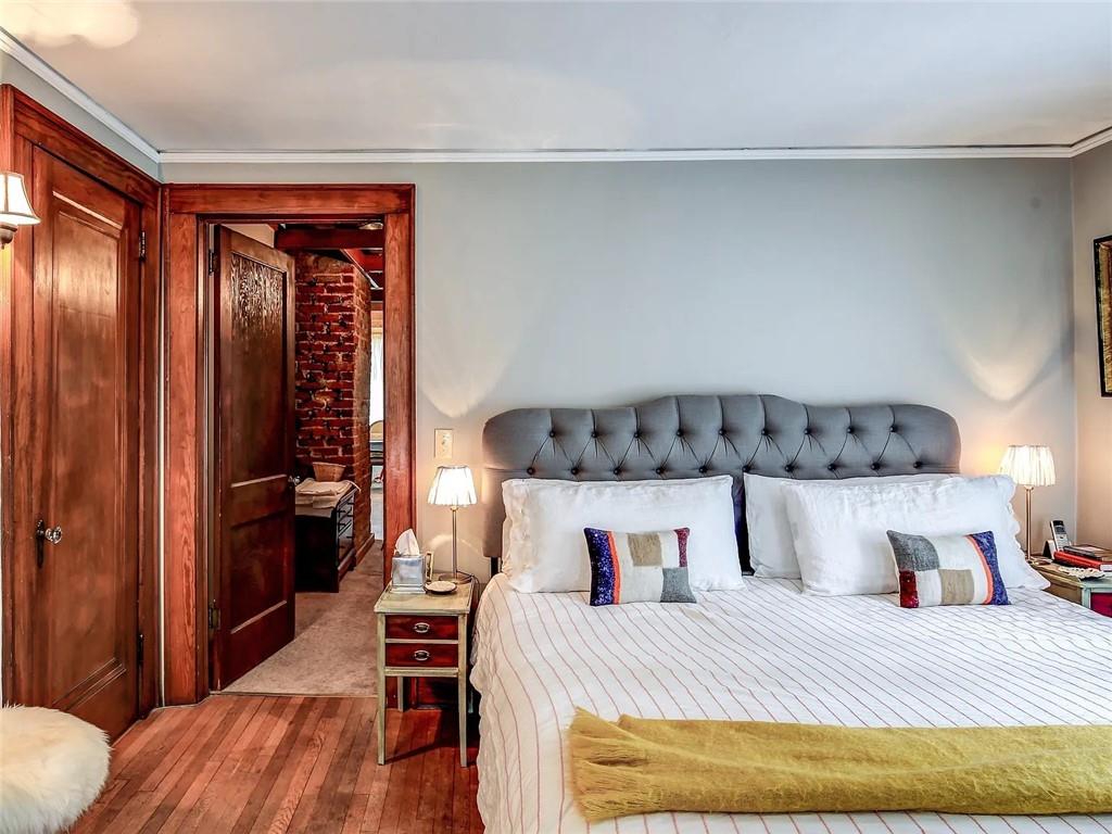 Bedroom with a gray tufted headboard, rich wood trim, and an exposed brick doorway.
