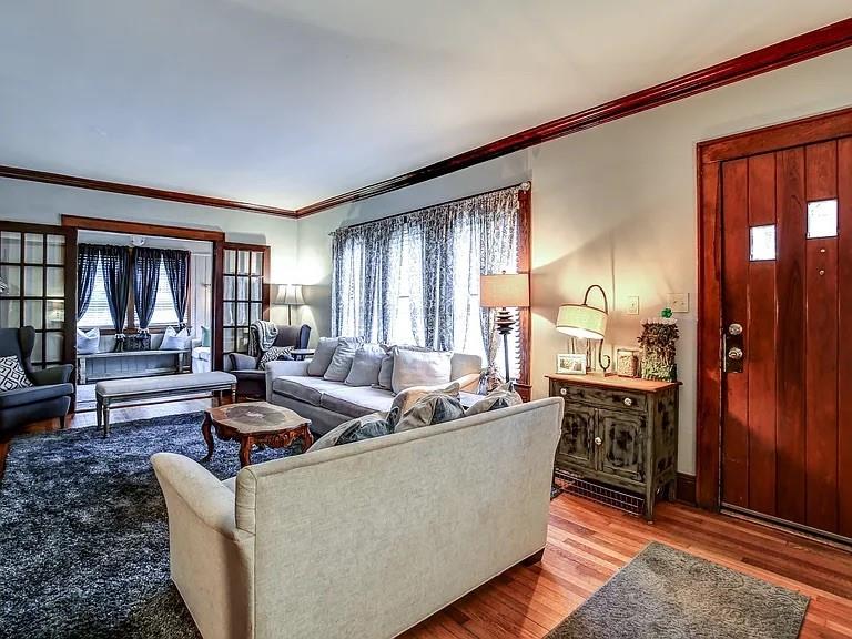 Living room with cream sofas, dark rug, hardwood floors, and a wooden entry door.