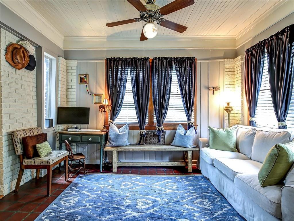 Living room with a white sofa, blue rug, and bench beneath curtained windows.