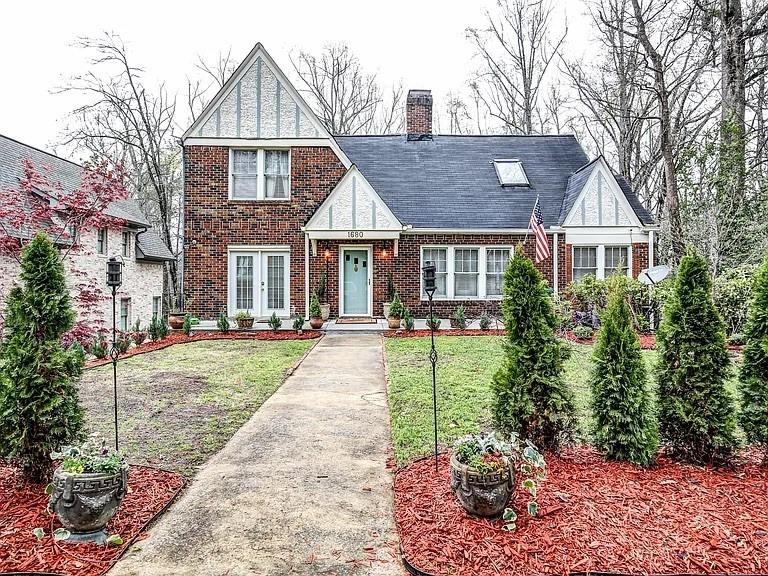 Brick home with white-trimmed gables, a front walkway, landscaped garden beds, and an American flag.