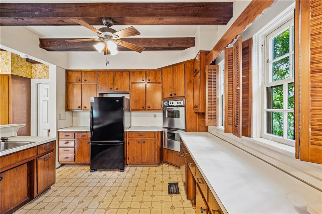 Kitchen with warm wood cabinetry, exposed beams, and a long counter beneath shuttered windows.