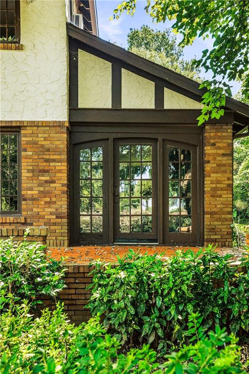 Home entrance with dark-framed glass doors, brick facade, and leafy shrubs.