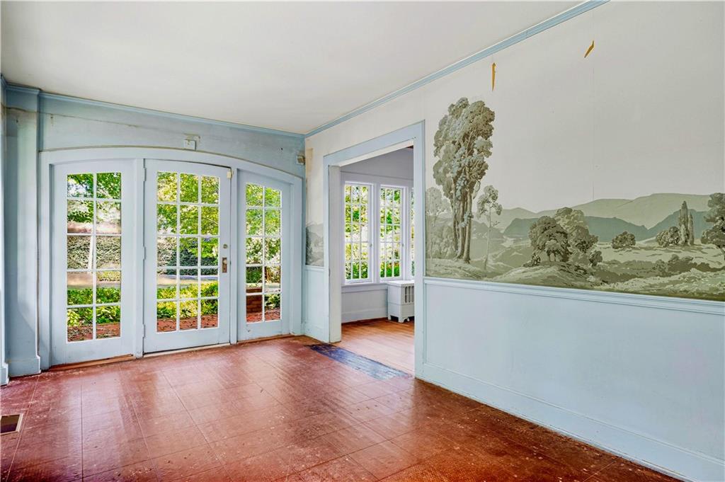 Bright sunroom with French doors, garden views, and a painted pastoral wall mural.