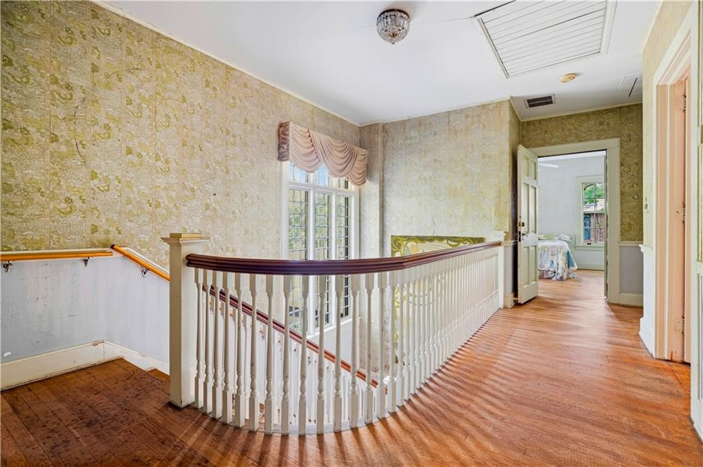 Upstairs landing with curved white balustrade, hardwood floors, and a bedroom visible through the doorway.