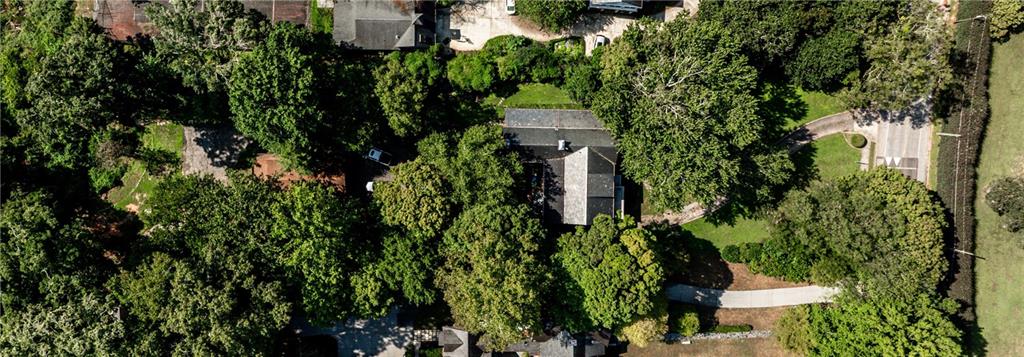 Aerial view of a tree-covered property with a house, curving driveway, and nearby paved court.