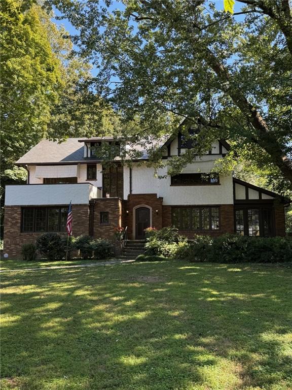 Two-story white and brick house with an arched entry, shaded by mature trees.