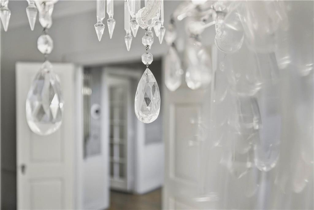 Crystal chandelier drops hang in the foreground of a bright interior with blurred white doorways.