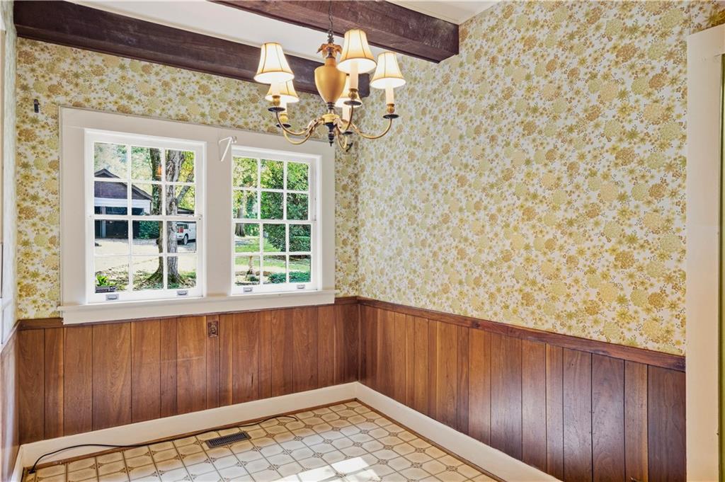 Empty dining room with floral wallpaper, wood wainscoting, and a chandelier.