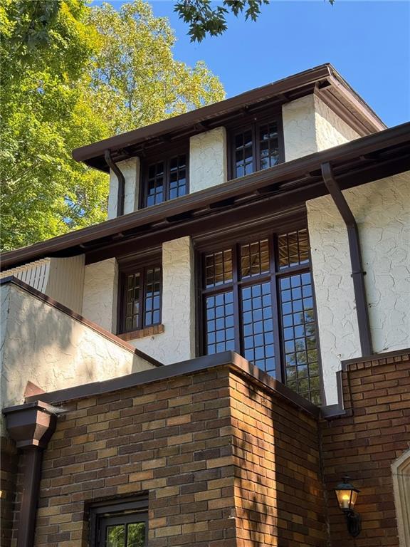 Home exterior with cream stucco, dark timber trim, tall gridded windows, and a brick facade.