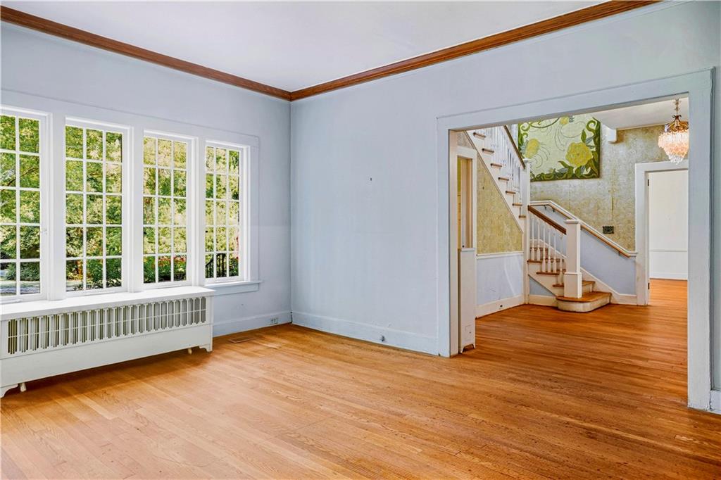 Empty room with hardwood floors and tall windows; an open doorway looks onto a staircase.