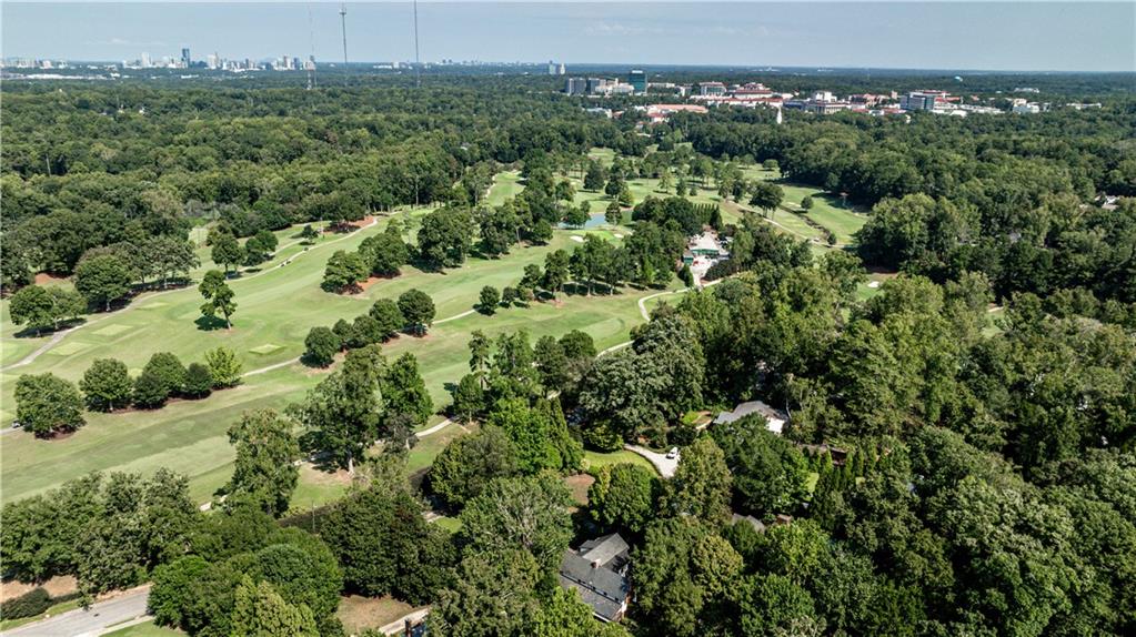 Aerial view of a tree-lined golf course with a distant city skyline.
