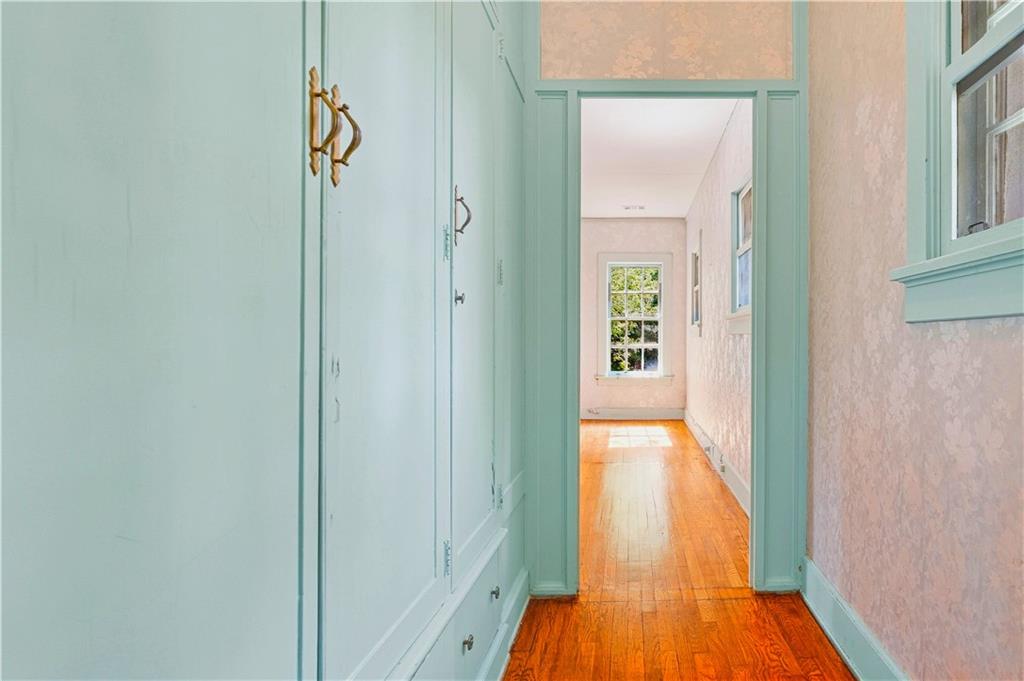 Hallway with pale aqua built-in cabinetry, blush walls, and polished hardwood floors.