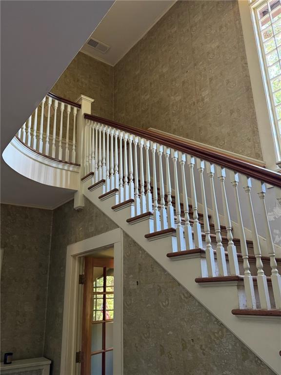 Foyer staircase with white balusters, dark wood rails, a curved landing, and a tall window.