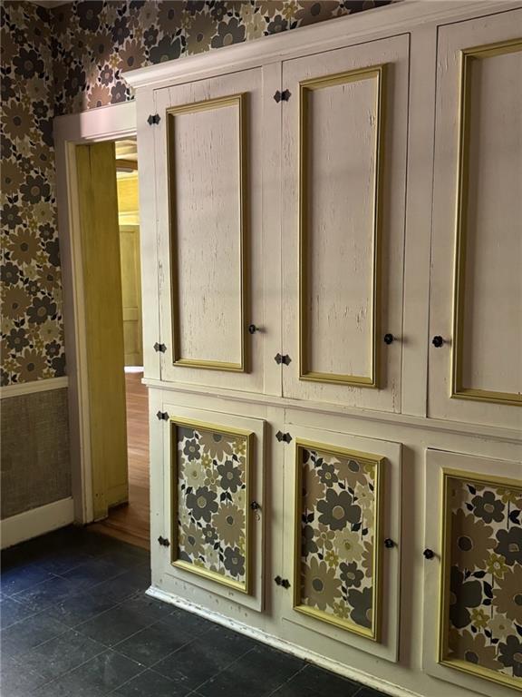 Cream built-in cabinets with brass trim and floral wallpaper panels beside a doorway.