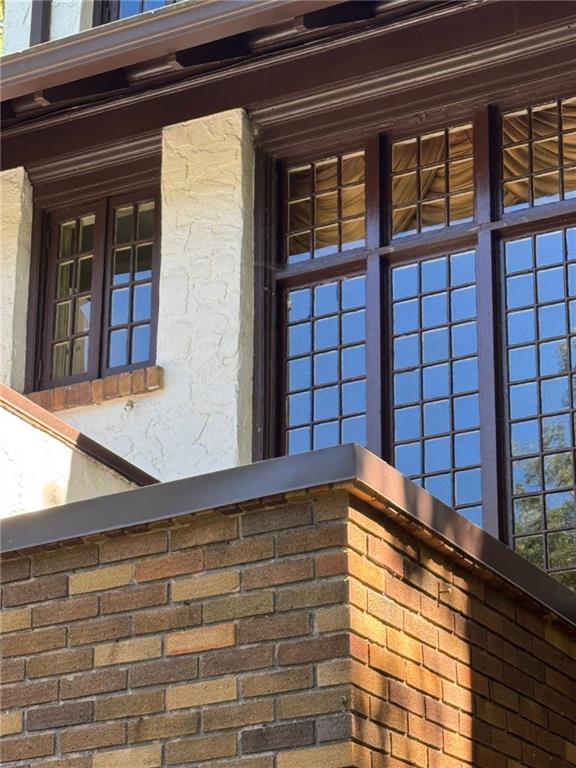 Home exterior with tall dark-framed windows above a brick parapet and cream stucco.