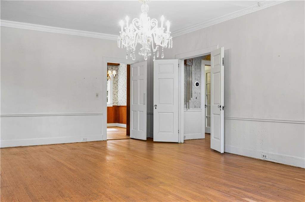 Empty room with hardwood floors, white paneled walls, a chandelier, and open doors.