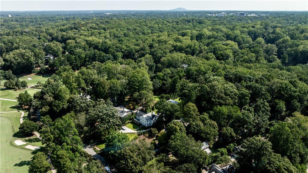 Aerial view of a white home surrounded by trees beside a golf course.