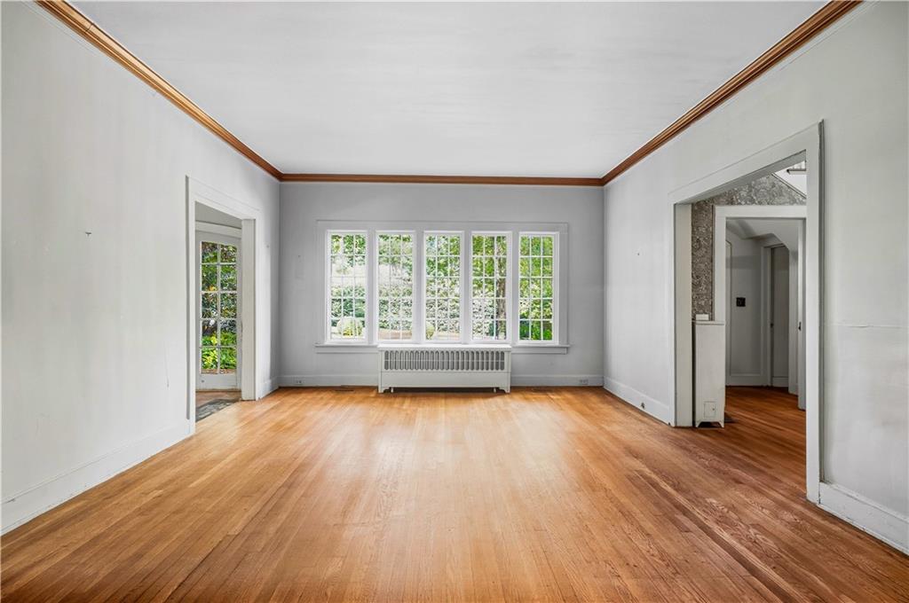 Empty room with hardwood floors, dark wood crown molding, and tall windows above a radiator.