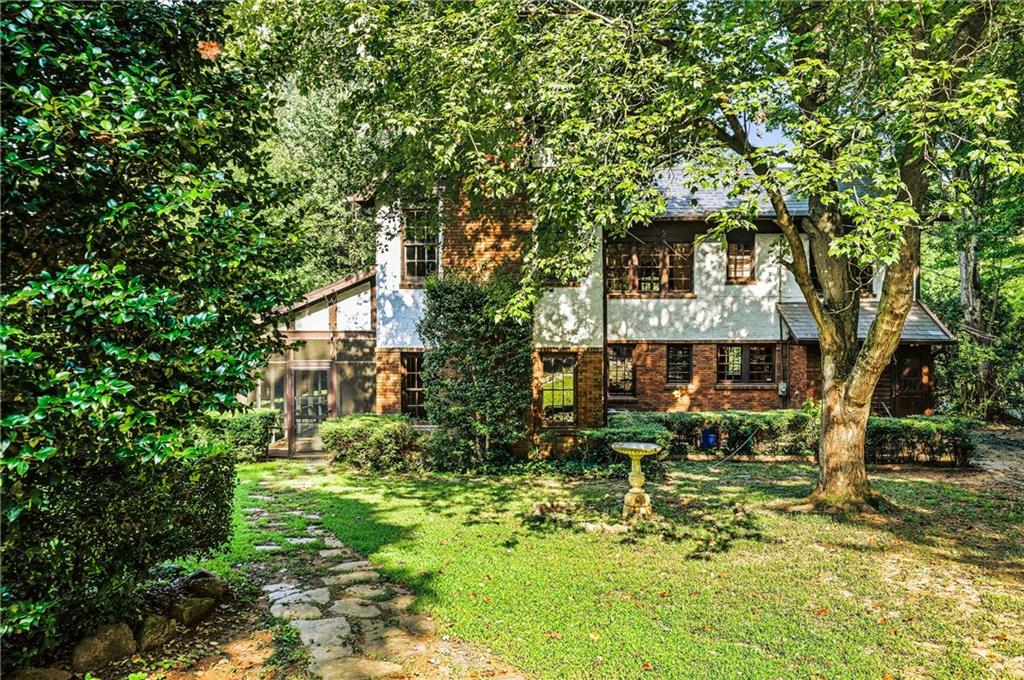 Two-story brick-and-stucco house shaded by mature trees, with a stone garden path and birdbath.