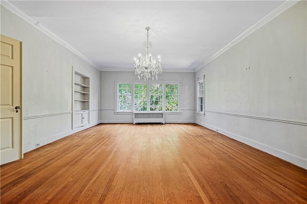 Vacant dining room with hardwood floors, chandelier, built-in shelves, and large windows.