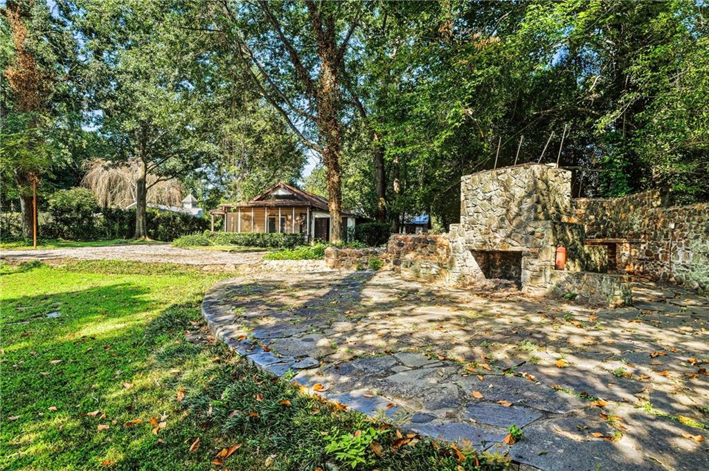 Wooded backyard with a stone patio, built-in outdoor fireplace, and screened porch.