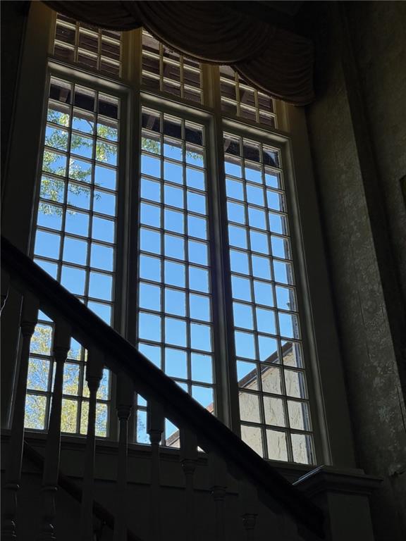 Staircase railing crosses tall multi-pane windows with blue sky and leafy trees outside.