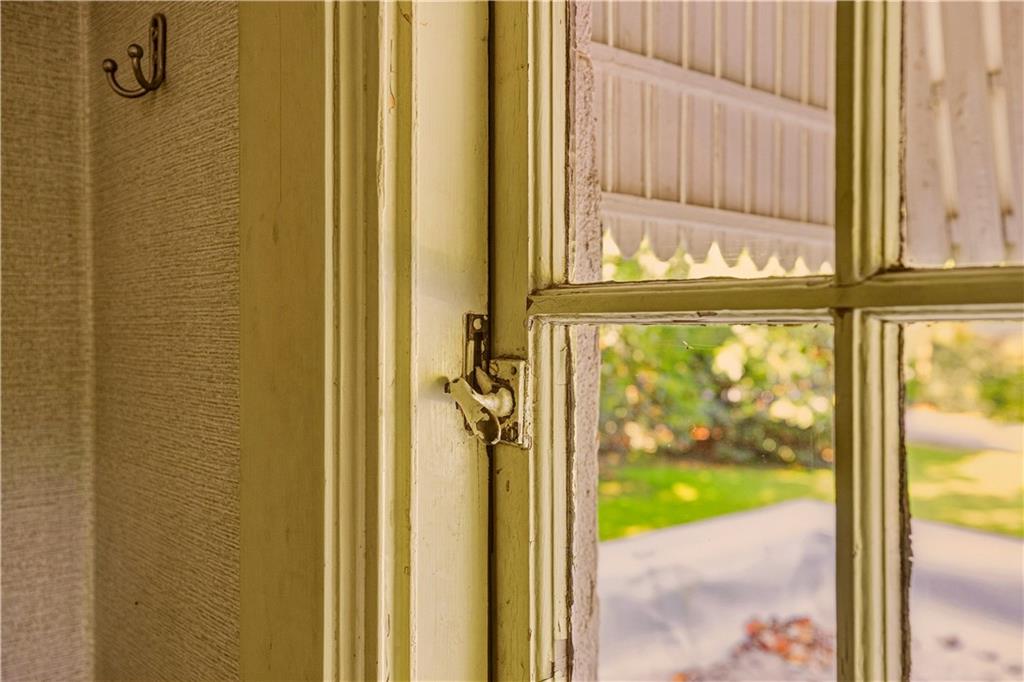 Window latch on a divided-light window overlooking a green lawn and paved path.