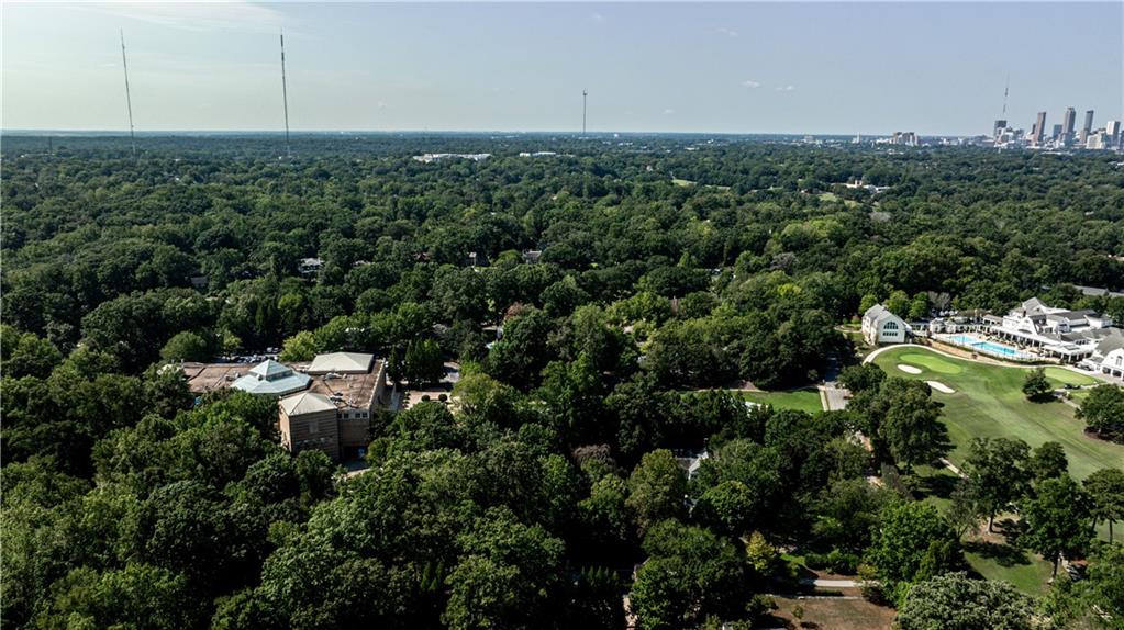 Aerial view over wooded Atlanta neighborhoods, a golf course, and the distant downtown skyline.