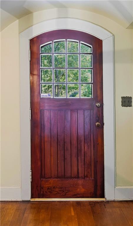 Arched dark wood entry door with divided glass panes and hardwood flooring.