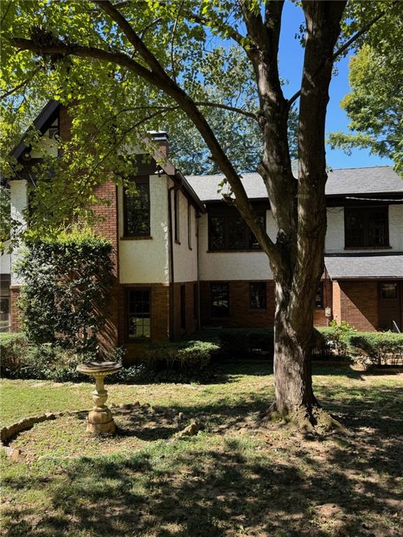 Two-story brick-and-siding home partly screened by a mature tree, with a birdbath in the front yard.