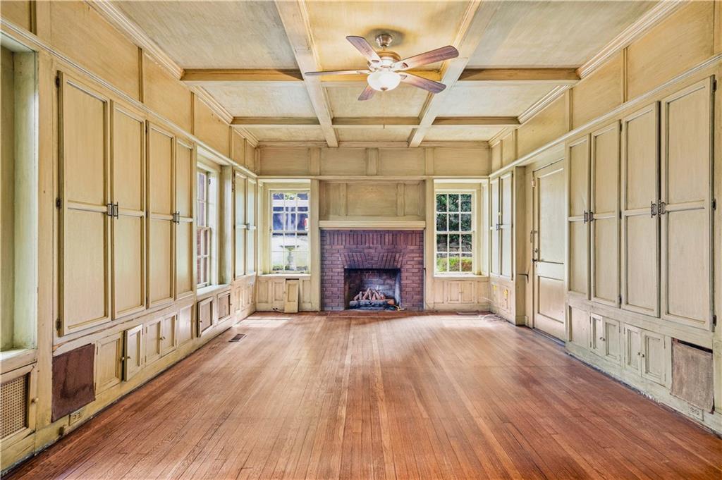 Wood-paneled living room with a brick fireplace, tall windows, and hardwood floors.